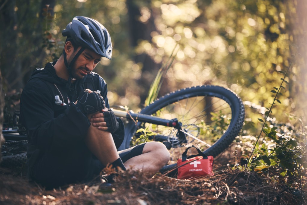 Ein Fahrradfahrer sitzt nach einem Sturz auf dem Waldboden neben seinem Fahrrad und hält sich das Knie