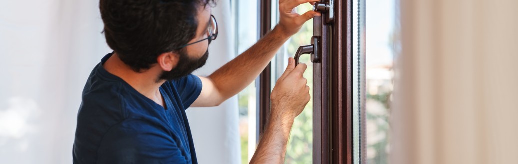 Ein Mann verschließt ein Fenster und trifft Vorkehrungen gegen einen Einbruch.