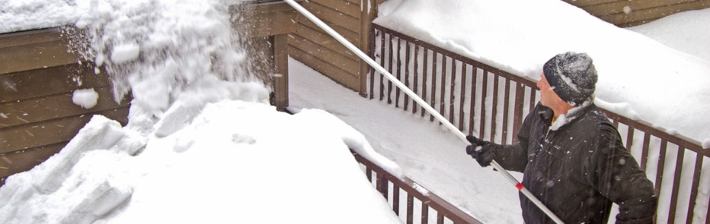 Ein Mann mit einem Schnee-Rechen entfernt Schnee vom Dach.