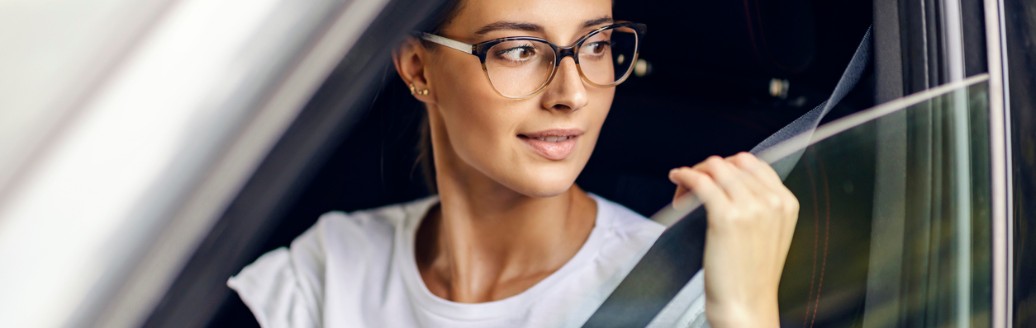 Eine junge Frau schnallt sich an und blickt dabei aus dem Autofenster.