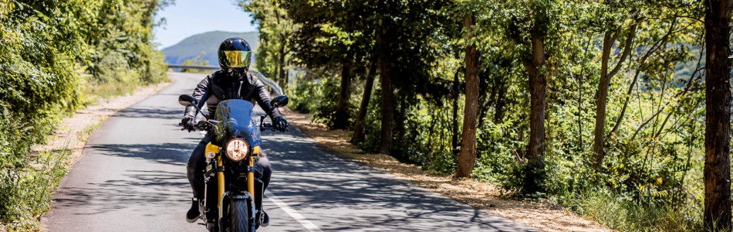 Ein Motorradfahrer fährt an einem sonnigen Tag eine Landstraße entlang.