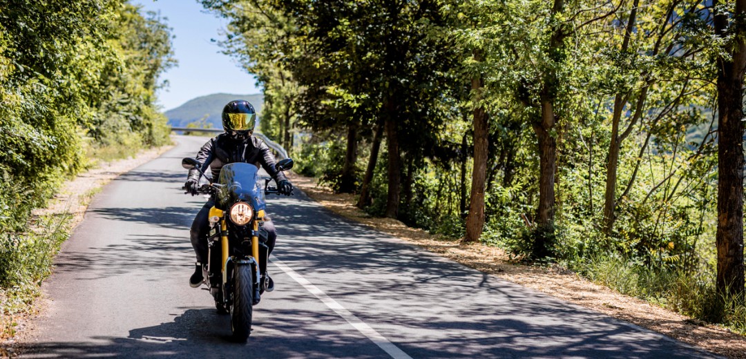 Ein Motorradfahrer fährt an einem sonnigen Tag eine Landstraße entlang.