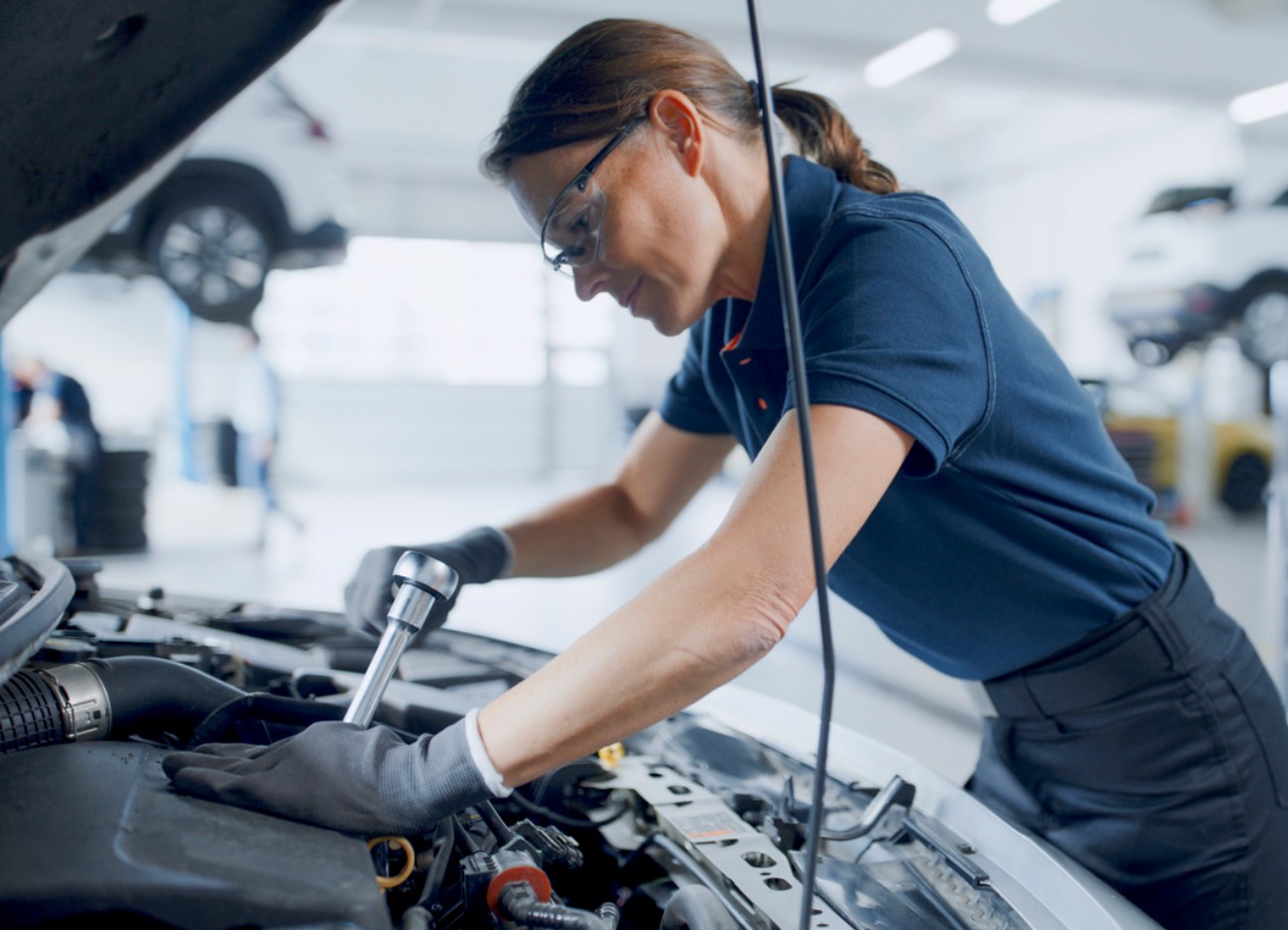 Eine Mechatronikerin schraubt an einem Automotor.