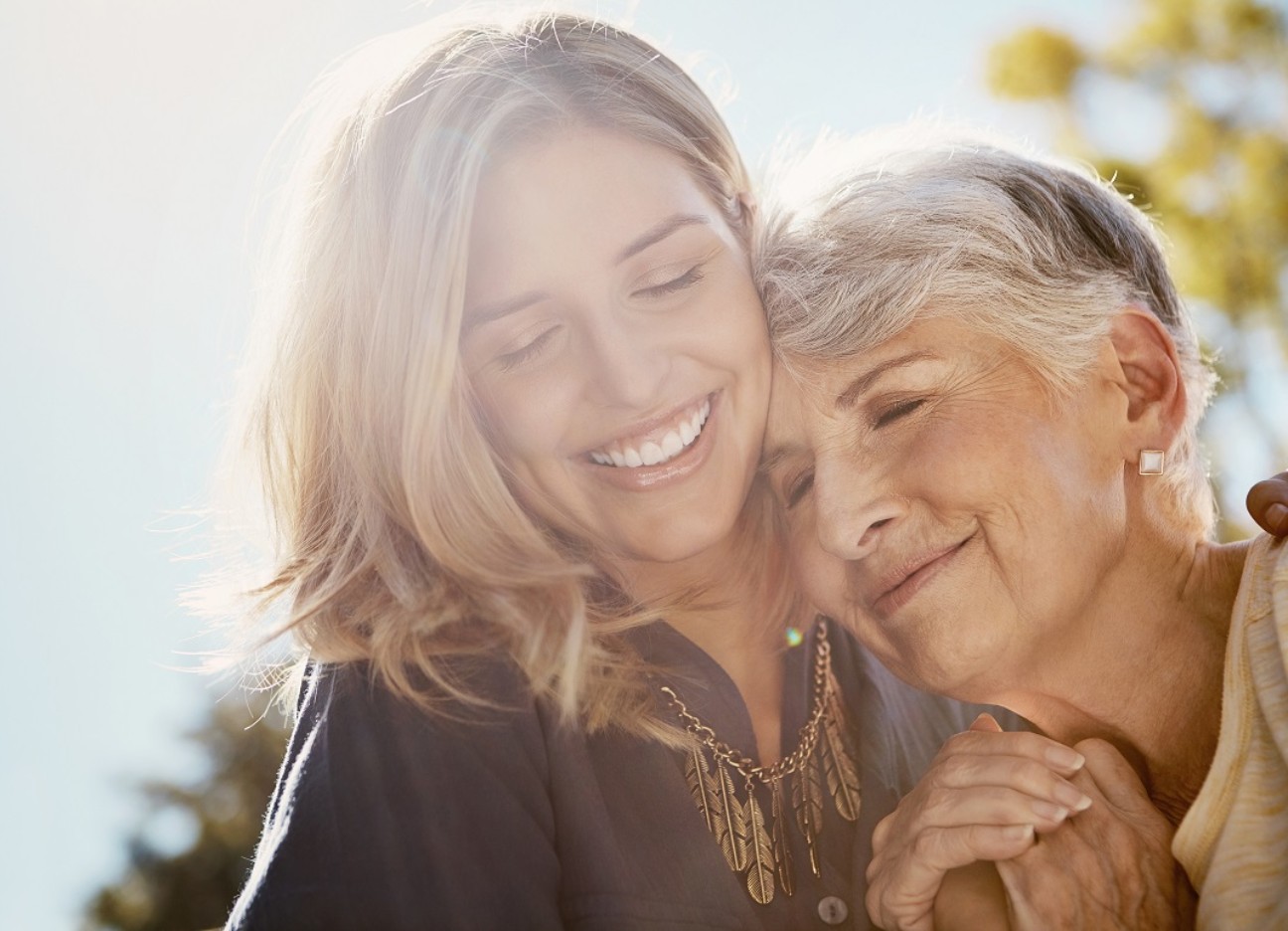 Ältere und jüngere Frau schmiegen sich lächelnd aneinander