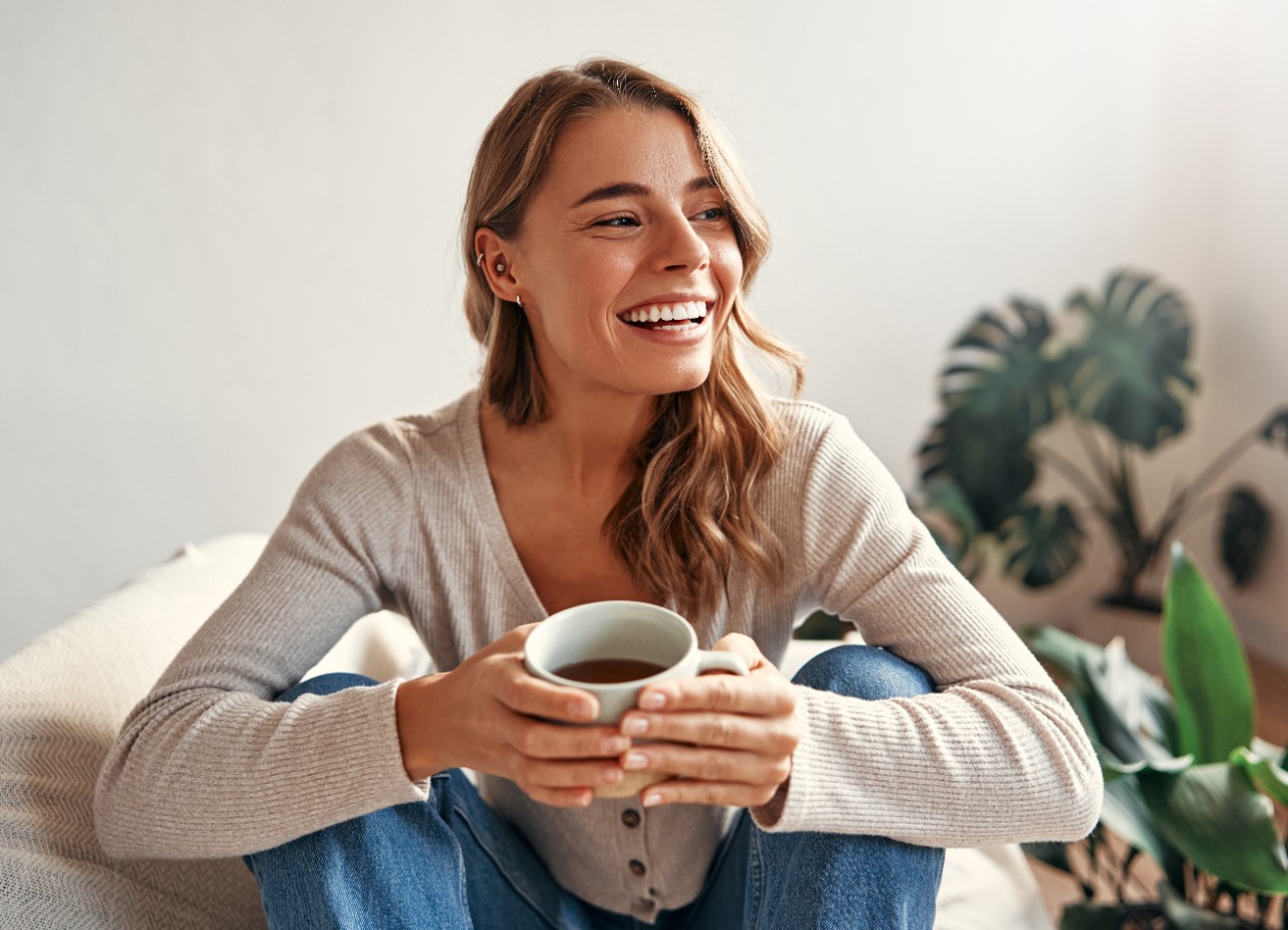 Eine Frau sitz lächelnd mit einer Tasse Kaffee auf dem Sofa