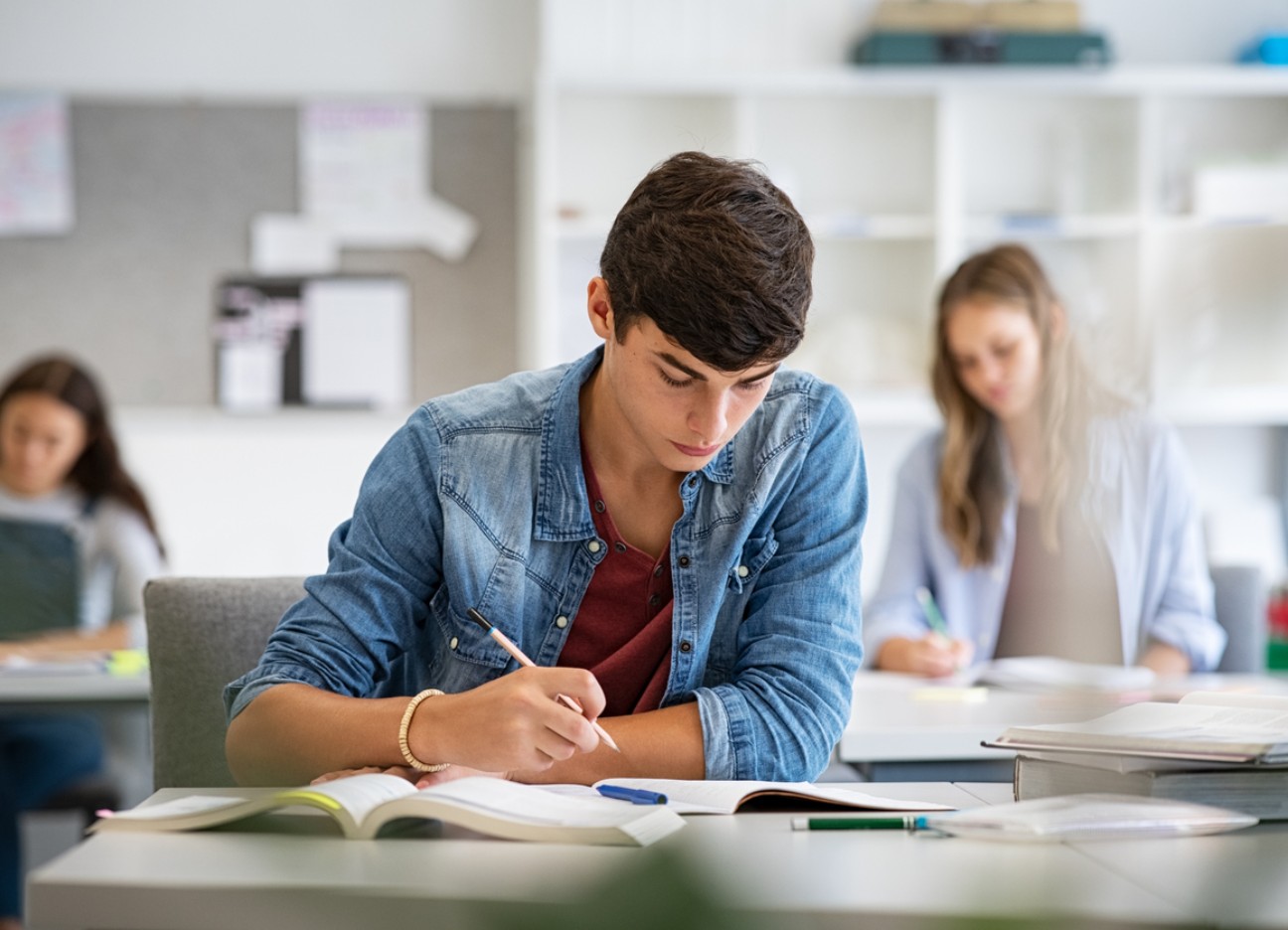 Ein Schüler der Sekundarstufe sitzt im Klassenzimmer an einem Tisch und schreibt etwas in seinen Block