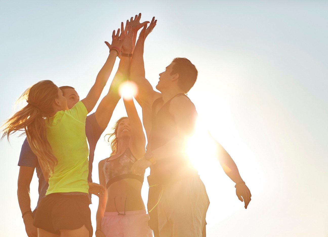 Sportler springen ins High-Five mit Sonne im Hintergrund