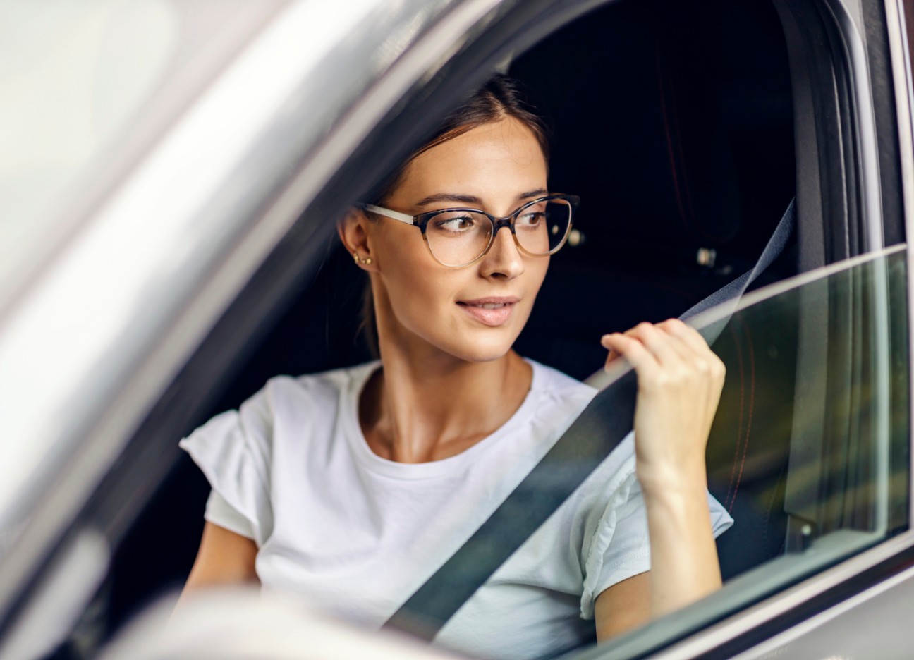 Eine junge Frau schnallt sich an und blickt dabei aus dem Autofenster.