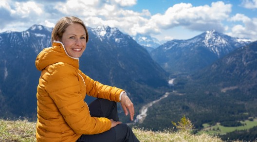 Magdalena Neuner sitzt auf einer Wiese in den Bergen und blickt in die Kamera.