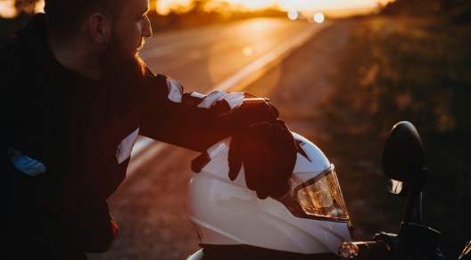 Motorradfahrer macht während einer Fahrt bei Sonnenuntergang eine Pause. Der Helm liegt auf dem Motorrad.