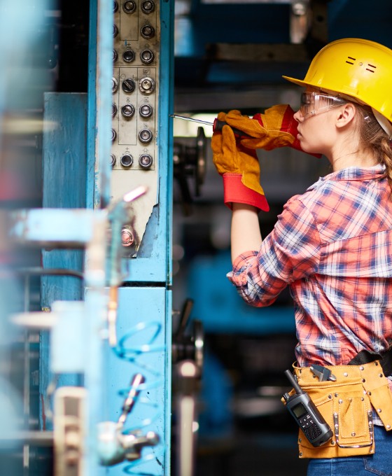 Eine junge Handwerkerin schraubt an einer Maschine. 