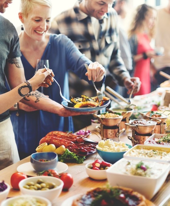 Mehrere Menschen stehen an einem vielseitigen, vollen Buffet.