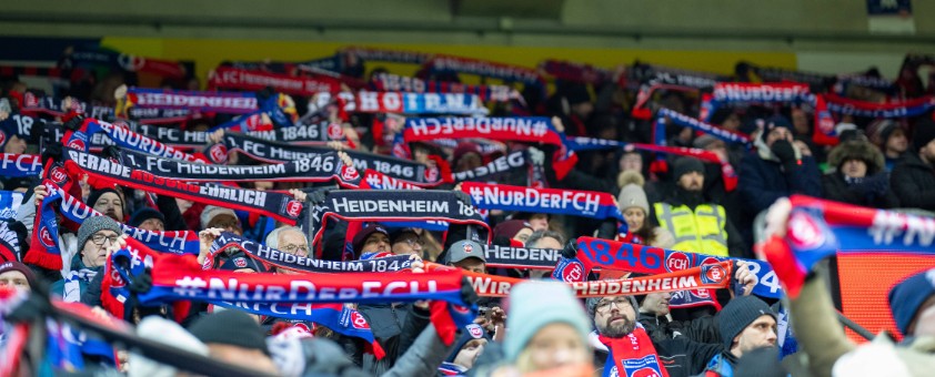 Viele Fans des FC Heidenheim auf der Tribüne des Stadions, wo sie ihre Fanschals hochhalten.