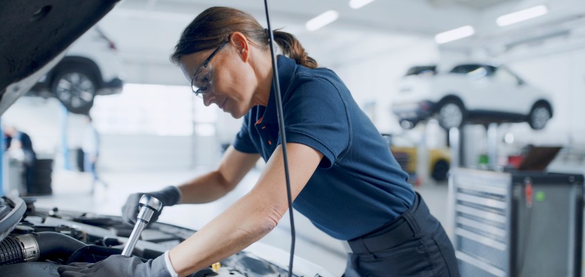 Eine Mechatronikerin schraubt an einem Automotor.