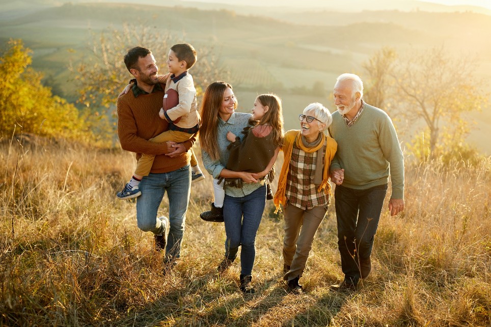 Glückliche Großfamilie, die beim Wandern am Herbsttag auf einem Hügel redet und lacht.