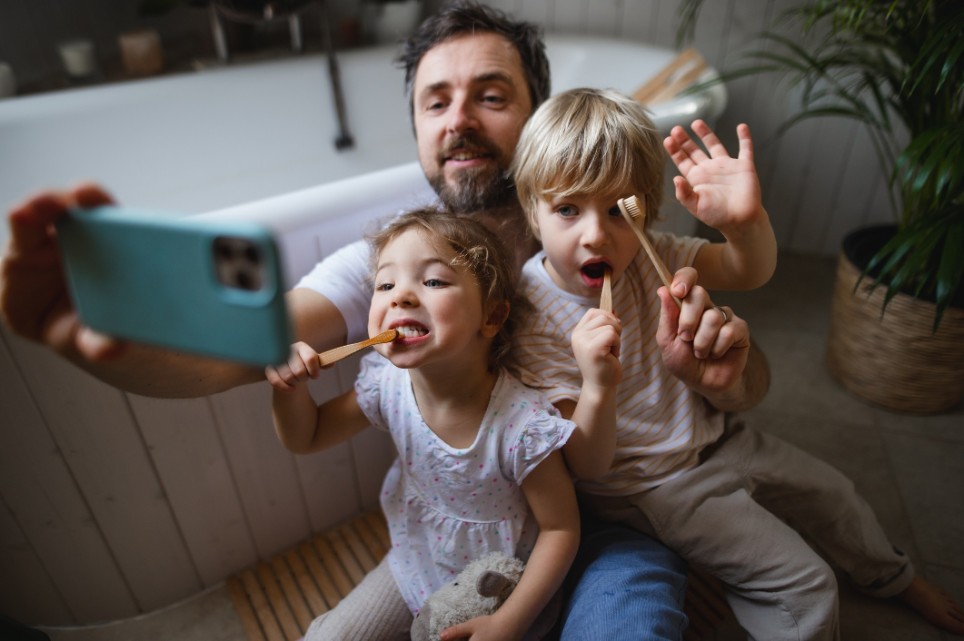 Ein Vater nimmt mit seiner Tochter und seinem Sohn ein Selfie auf, während sie beide am Zähne putzen sind.