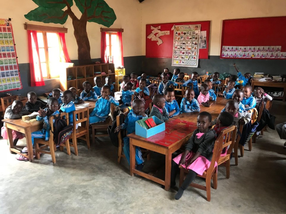 Kleine Schülerinnen und Schüler sitzen in einem Klassenzimmer in Isele, Tansania und blicken freudig in die Kamera.