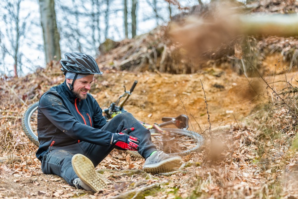 Mann sitzt nach Mountainbikeunfall mit Schmerzen auf dem Boden