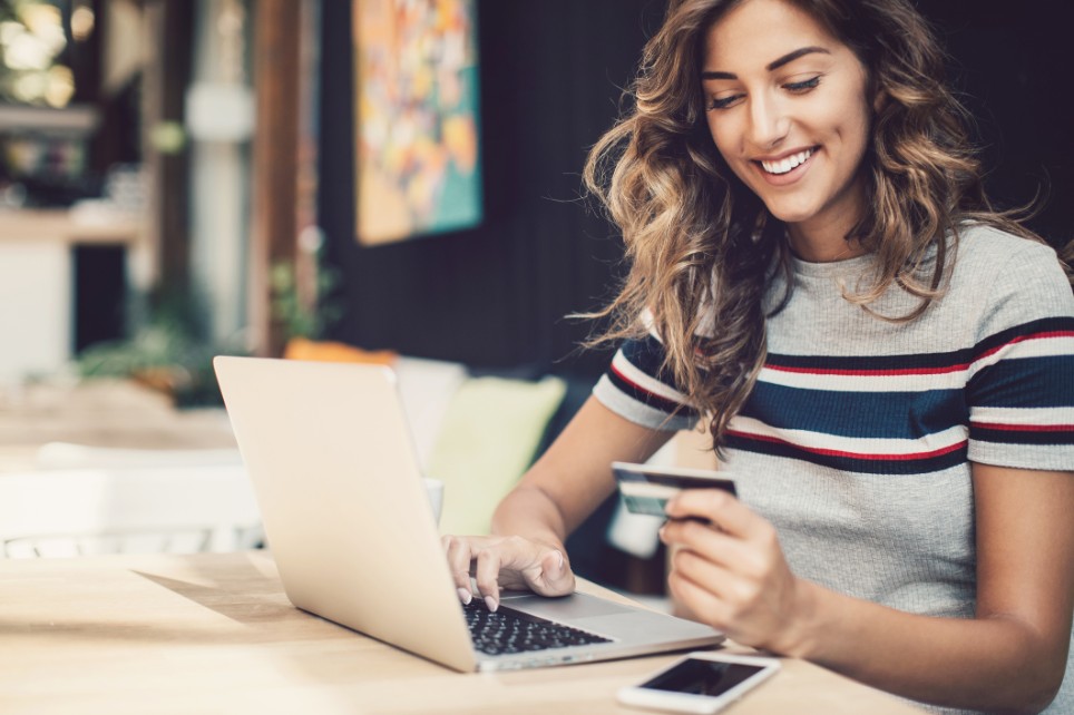 Lächelnde junge Frau mit Kreditkarte tippt in einen Laptop