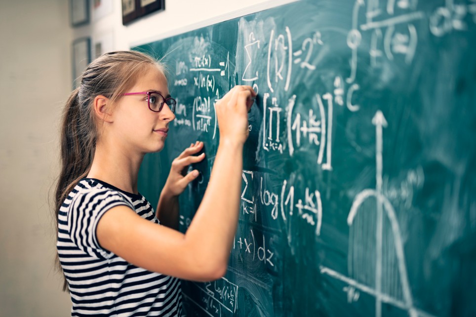 Eine Schülerin mit Brille schreibt mathematische Formeln an die Tafel