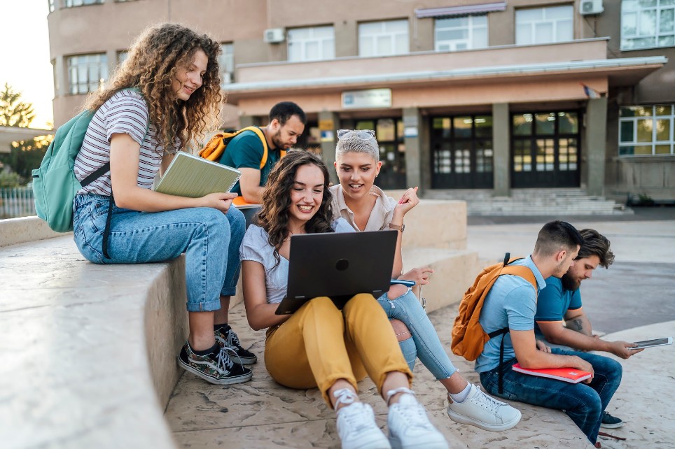 Gruppe von Studenten, die draußen sitzen, abhängen, reden und Laptops benutzen.