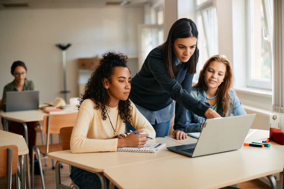 Eine Lehrerin zeigt zwei Schülerinnen etwas auf einem Laptop